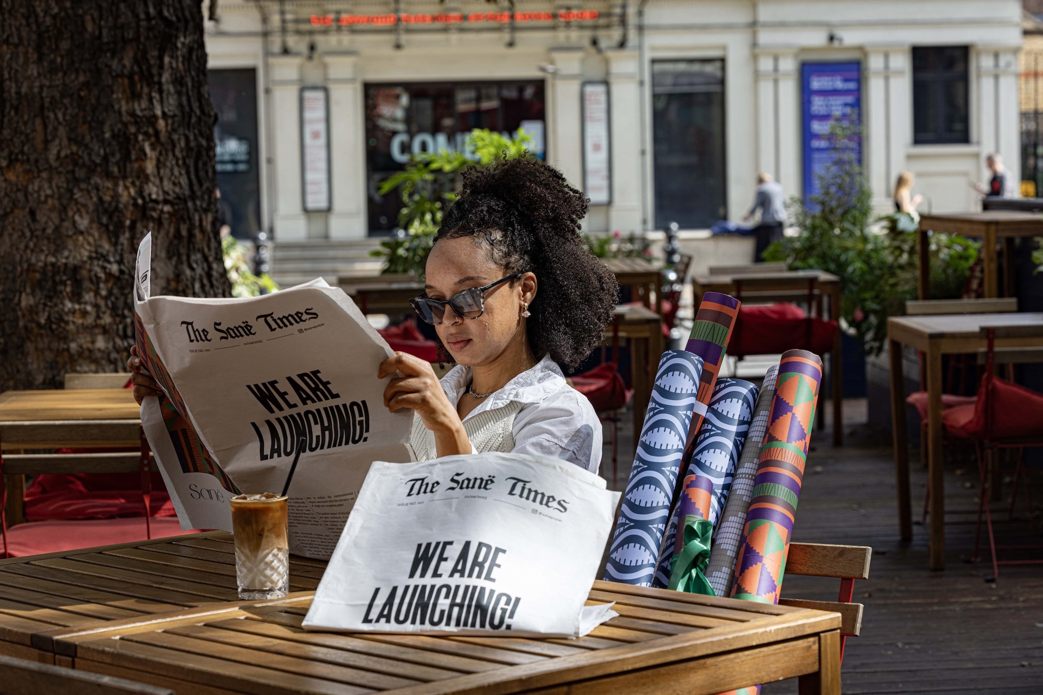 Model poses with Sanë newspaper & iced coffee, in a courtyard next to the various Sanë wrapping paper